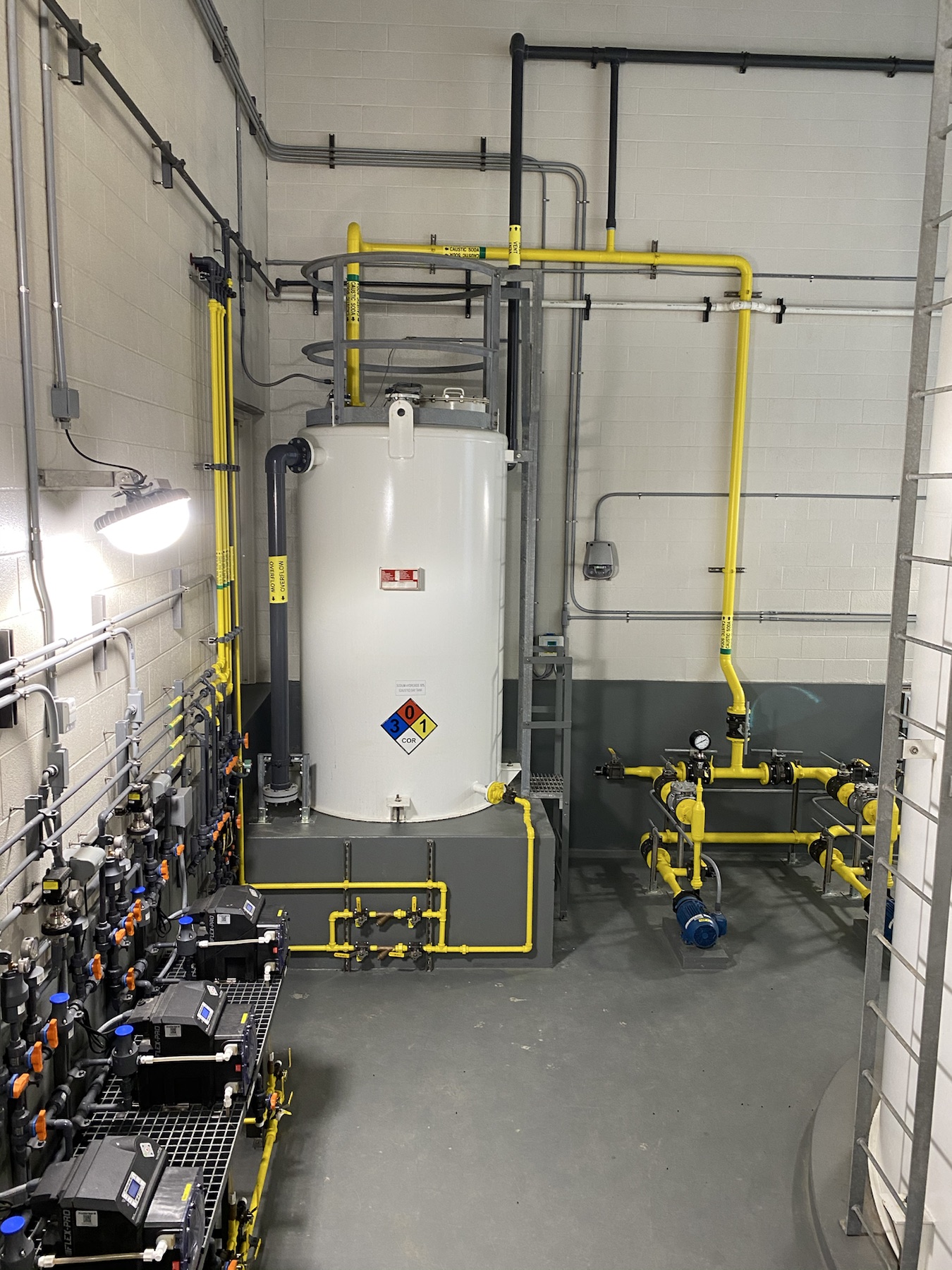 Clean chemical feed room with yellow piping, storage tank, and metering equipment